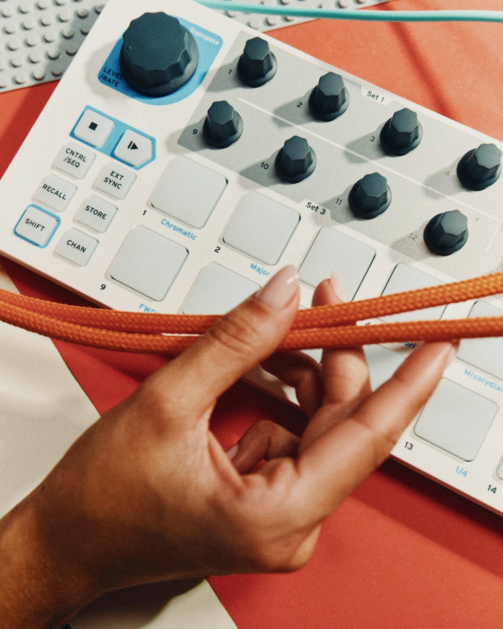 A hand on a drum machine with an orange cable